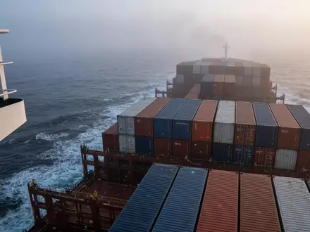 Ein großes Containerschiff auf stürmischer See bei Dämmerung, symbolisch für globale Handelsrouten und Marktunsicherheit. - Foto: über boerse-global.de