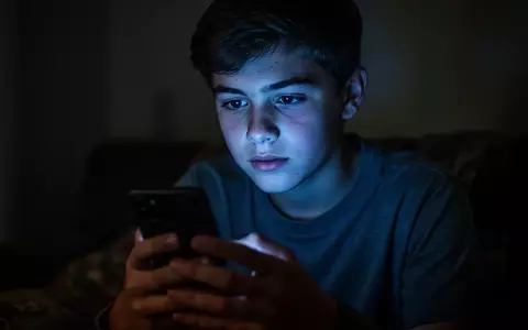 Ein Jugendlicher schaut in einem abgedunkelten Raum auf den hell leuchtenden Bildschirm eines Smartphones. - Foto: über boerse-global.de