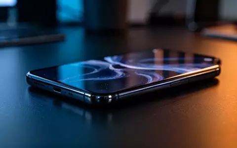 Ein modernes Smartphone liegt auf einem dunklen Schreibtisch in einer professionellen Büroumgebung bei gedimmtem Licht. - Foto: über boerse-global.de