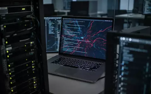 Ein Laptop-Bildschirm zeigt abstrakte Codezeilen in einem dunklen Büro, was auf IT-Sicherheitsrisiken und Cyberangriffe hindeutet. - Foto: über boerse-global.de