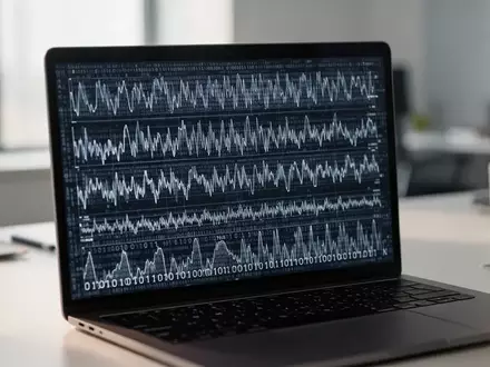 Ein moderner Arbeitsplatz mit einem Laptop, auf dessen Bildschirm abstrakte Datenmuster und statistische Strukturen zu sehen sind. - Foto: über boerse-global.de