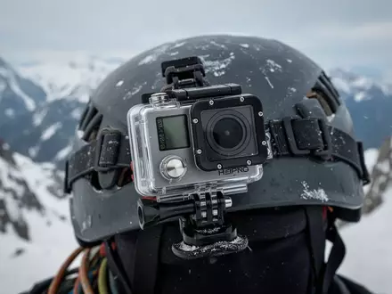 Eine Actionkamera montiert auf einem Kletterhelm vor einer verschneiten Bergkulisse. - Foto: über boerse-global.de