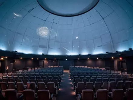 Innenansicht eines modernen Planetariums mit einer großen Kuppeldecke und Reihen von Sitzplätzen in gedimmtem Licht. - Foto: über boerse-global.de