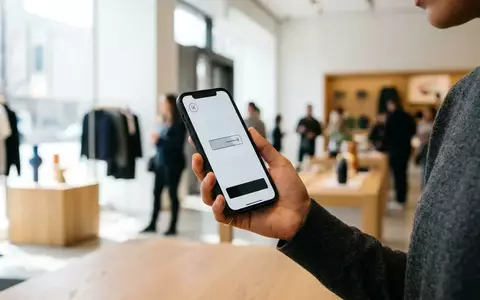 Eine Hand hält ein Smartphone in einer hellen Einzelhandelsumgebung, während ein digitaler Bezahlvorgang stattfindet. - Foto: über boerse-global.de