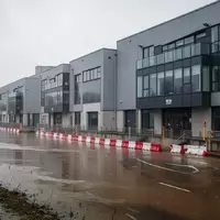Moderne Industriegebäude mit Hochwasserschutzbarrieren an einem Flussufer bei bewölktem Himmel. - Foto: über boerse-global.de