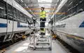 Ein Techniker arbeitet auf einer mobilen Wartungsplattform an einem Schienenfahrzeug in einer modernen Werkstatt. - Foto: über boerse-global.de