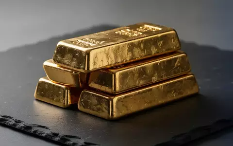 Ein Stapel glänzender Goldbarren auf einer dunklen Schieferplatte bei natürlichem, kinematografischem Licht. - Foto: über boerse-global.de