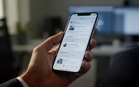Eine Hand hält ein Smartphone in einer Büroumgebung, während der Nutzer auf einem unscharfen Display eine Nachricht betrachtet. - Foto: über boerse-global.de