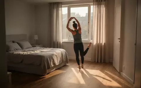 Eine Person führt bei sanftem Morgenlicht in einem minimalistischen Schlafzimmer leichte Dehnübungen aus. - Foto: über boerse-global.de