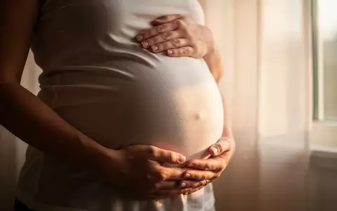 Nahaufnahme der Hände einer schwangeren Frau, die sanft ihren Bauch halten, in weichem Tageslicht. - Foto: über boerse-global.de