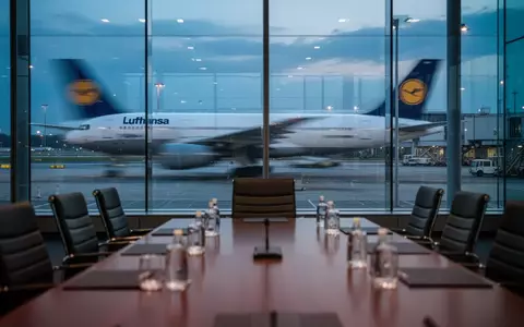 Ein Konferenztisch vor einem Fenster mit Blick auf ein Lufthansa-Flugzeug auf dem Rollfeld bei Dämmerung. - Foto: über boerse-global.de