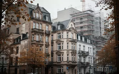 Ein älteres Wohnhaus in einem dicht bebauten Stadtviertel unter bewölktem Himmel. - Foto: über boerse-global.de