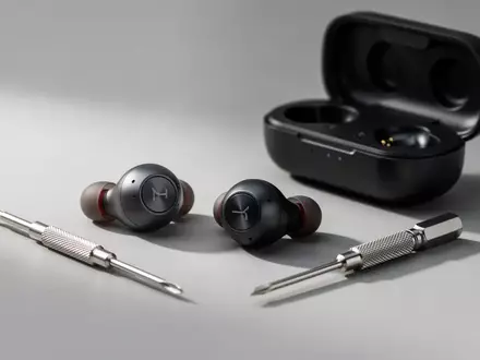 Hochwertige kabellose In-Ear-Kopfhörer liegen neben einem kleinen Präzisionsschraubendreher und einem Ladecase auf einem Tisch. - Foto: über boerse-global.de