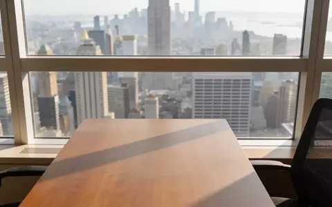 Ein moderner Schreibtisch in einem hellen Büro mit Blick auf eine verschwommene Skyline bei Tageslicht. - Foto: über boerse-global.de