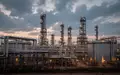 Industrielle Raffinerieanlagen bei Dämmerung mit komplexen Rohrleitungen und Speichertanks vor einem bewölkten Himmel. - Foto: über boerse-global.de