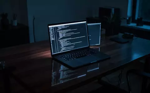 Ein minimalistischer Arbeitsplatz mit einem Laptop, auf dem abstrakte Programmiercodes in einem dunklen Raum zu sehen sind. - Foto: über boerse-global.de