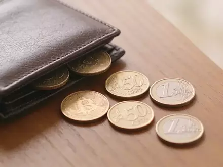 Nahaufnahme einer minimalistischen Schreibtischoberfläche mit einer Geldbörse und einigen verstreuten Münzen bei natürlichem Licht. - Foto: über boerse-global.de