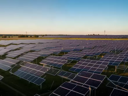 Weitläufiger Solarpark mit zahlreichen Photovoltaikmodulen in einer grünen Landschaft bei Sonnenuntergang. - Foto: über boerse-global.de