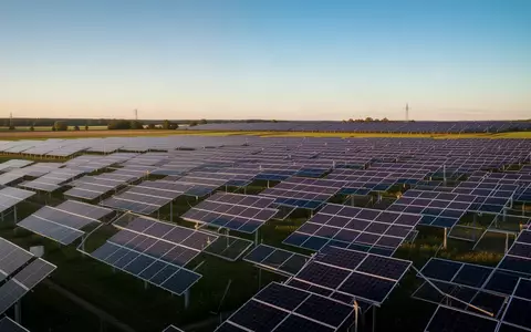 Weitläufiger Solarpark mit zahlreichen Photovoltaikmodulen in einer grünen Landschaft bei Sonnenuntergang. - Foto: über boerse-global.de