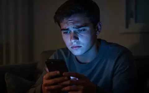 Eine nachdenklich wirkende junge Person blickt in einem abgedunkelten Raum auf den Bildschirm ihres Smartphones. - Foto: über boerse-global.de