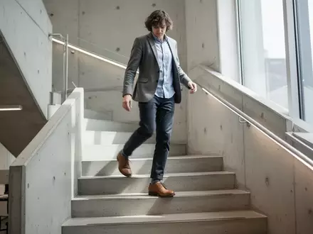 Eine Person in Business-Kleidung beim Treppensteigen in einem modernen Bürogebäude bei Tageslicht. - Foto: über boerse-global.de