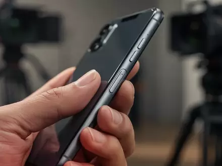 Nahaufnahme einer Hand, die ein modernes iPhone hält, mit Fokus auf die physische Kamerataste an der Gehäuseseite. - Foto: über boerse-global.de