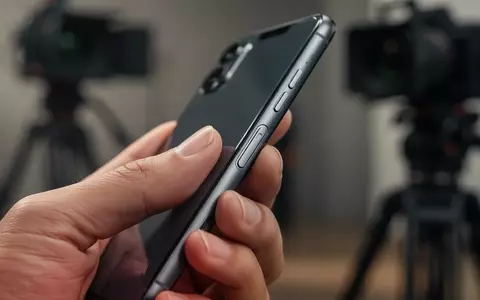 Nahaufnahme einer Hand, die ein modernes iPhone hält, mit Fokus auf die physische Kamerataste an der Gehäuseseite. - Foto: über boerse-global.de