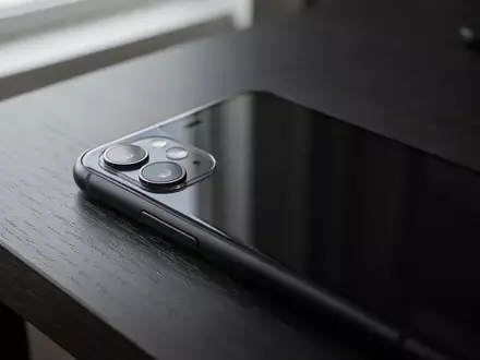 Ein modernes Smartphone liegt auf einem dunklen Holztisch in einer professionell ausgeleuchteten Umgebung. - Foto: über boerse-global.de