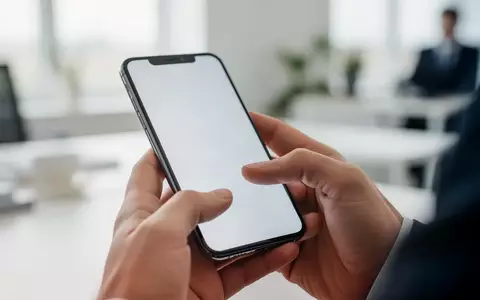 Nahaufnahme einer Hand, die ein Smartphone in einer modernen Büroumgebung hält, um eine App zu bedienen. - Foto: über boerse-global.de