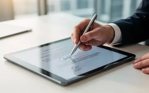 Eine Person unterschreibt digital einen Vertrag auf einem Tablet in einem modernen Büro. - Foto: über boerse-global.de