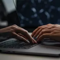 Hände eines Mitarbeiters an einer Computertastatur in einem professionellen Bürogebäude bei gedimmtem Licht. - Foto: über boerse-global.de