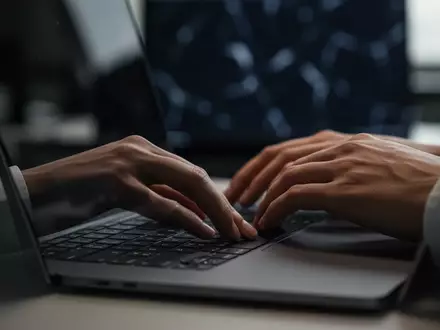 Hände eines Mitarbeiters an einer Computertastatur in einem professionellen Bürogebäude bei gedimmtem Licht. - Foto: über boerse-global.de