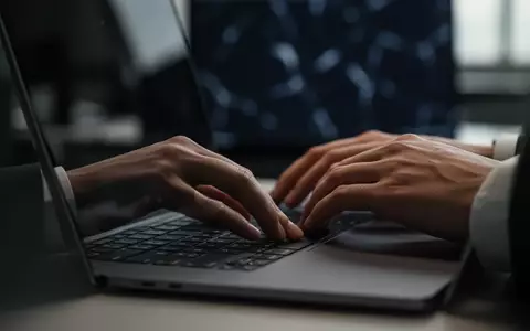 Hände eines Mitarbeiters an einer Computertastatur in einem professionellen Bürogebäude bei gedimmtem Licht. - Foto: über boerse-global.de