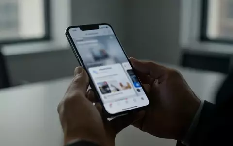 Person hält ein Smartphone in einer dezent beleuchteten Büroumgebung, Fokus auf die Hände und das Display des Geräts. - Foto: über boerse-global.de