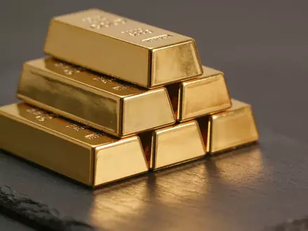 Mehrere glänzende Goldbarren auf einer dunklen, strukturierten Oberfläche bei warmem Licht. - Foto: über boerse-global.de