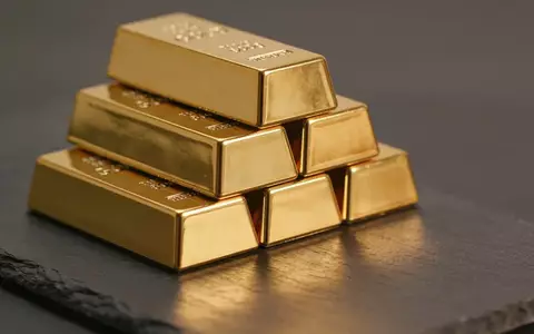 Mehrere glänzende Goldbarren auf einer dunklen, strukturierten Oberfläche bei warmem Licht. - Foto: über boerse-global.de