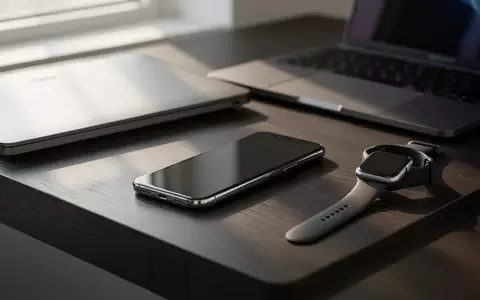 Ein minimalistischer Arbeitsplatz mit einem Smartphone, einer Smartwatch und einem Laptop auf einem dunklen Holztisch. - Foto: über boerse-global.de