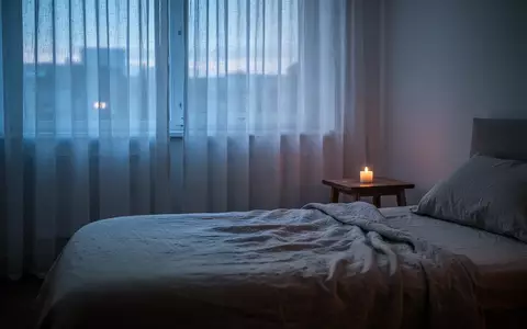 Minimalistisches Schlafzimmer in gedimmtem Abendlicht mit einem unangezündeten Kerzenlicht auf einem Nachttisch. - Foto: über boerse-global.de