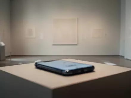 Ein unscharfes Smartphone liegt auf einem Podest vor einer leeren Museums-Ausstellungswand. - Foto: über boerse-global.de