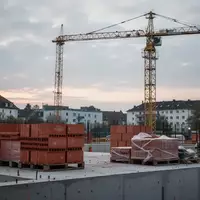 Eine verlassene Baustelle mit einem unbesetzten Baukran und gestapelten Baumaterialien vor einem bewölkten Himmel. - Foto: über boerse-global.de