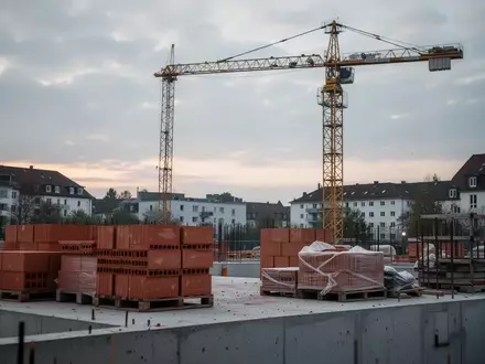 Eine verlassene Baustelle mit einem unbesetzten Baukran und gestapelten Baumaterialien vor einem bewölkten Himmel. - Foto: über boerse-global.de