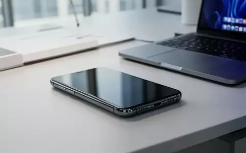 Ein modernes Smartphone liegt neben einem Laptop auf einem Schreibtisch in einem hellen Büro. - Foto: über boerse-global.de