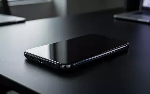 Ein modernes Smartphone liegt auf einem dunklen Büroschreibtisch in einer professionellen, minimalistischen Umgebung. - Foto: über boerse-global.de