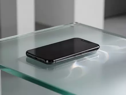 Ein modernes Smartphone auf einer mattierten Glasoberfläche mit sanften Lichtbrechungen in einer minimalistischen Umgebung. - Foto: über boerse-global.de