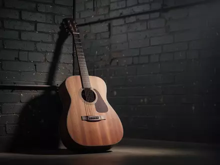 Eine akustische Gitarre lehnt an einer industriellen Backsteinwand in einem stimmungsvoll beleuchteten Studio. - Foto: über boerse-global.de