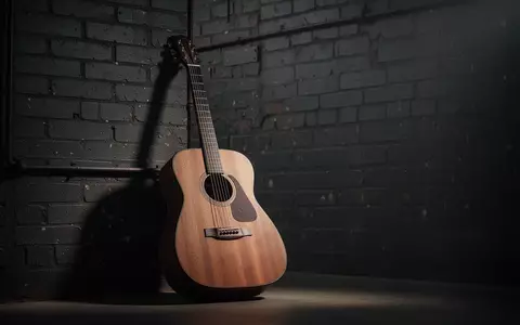 Eine akustische Gitarre lehnt an einer industriellen Backsteinwand in einem stimmungsvoll beleuchteten Studio. - Foto: über boerse-global.de
