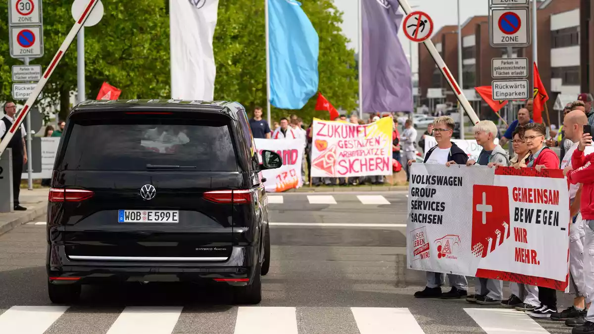 Ein VW-Bus mit VW-Vorstandschef Oliver Blume passiert die Demonstration von Beschäftigten am Werkstor des Standortes Zwickau.  - Bild: Hendrik Schmidt/dpa