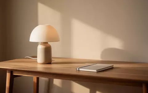 Ein minimalistischer, ruhiger Arbeitsplatz mit einer unbeleuchteten Lampe und einem geschlossenen Notizbuch in sanftem Licht. - Foto: über boerse-global.de