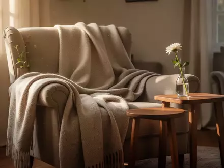 Ein sonnendurchflutetes, ruhiges Wohnzimmer mit einem gemütlichen Sessel, einer Wolldecke und einer einzelnen Blume in einer Vase. - Foto: über boerse-global.de