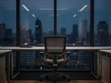 Ein leerer Büroarbeitsplatz vor einer dunklen Fensterfront mit Blick auf eine verschwommene Stadt bei Dämmerung. - Foto: über boerse-global.de